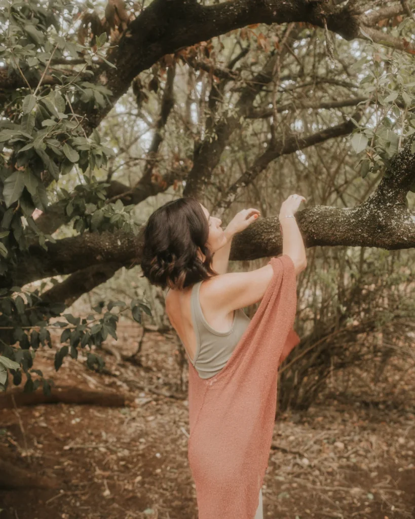 Tania Fernández en medio del bosque sujetando un árbol, reflejando pureza y vibras espirituales elevadas