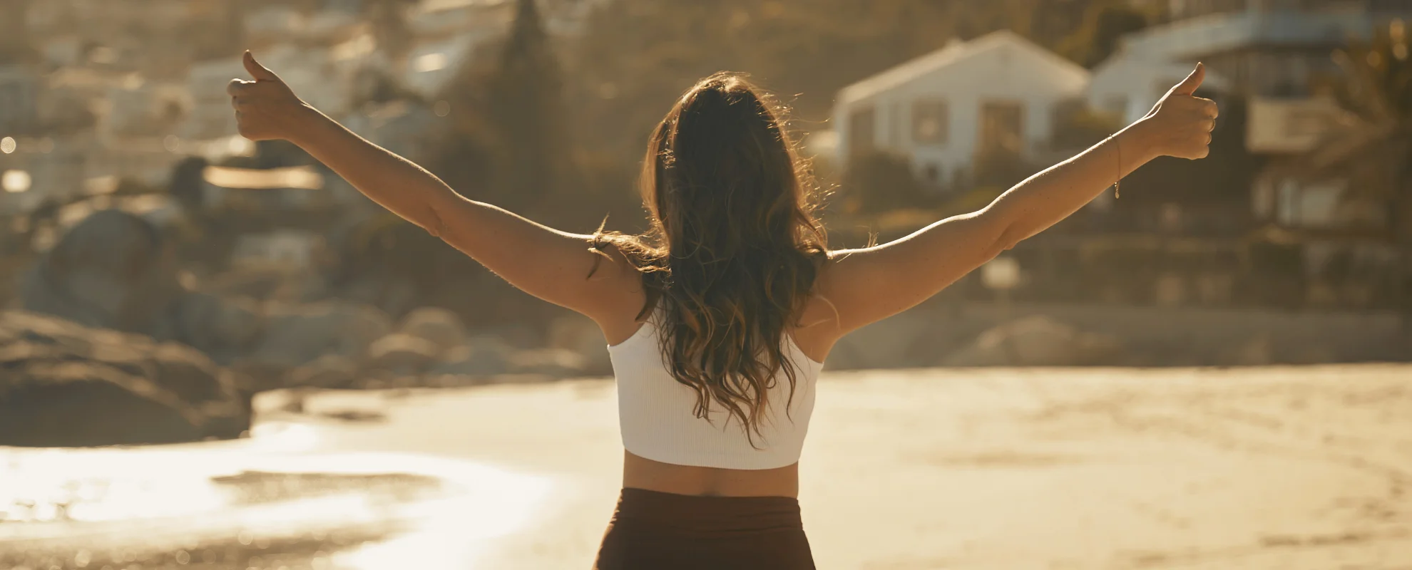 Mujer con los brazos abiertos hacia el cielo, disfrutando de un paisaje natural al atardecer, representando libertad, bienestar y psicología positiva.