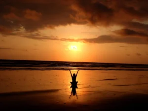 Silueta de una persona con los brazos extendidos frente al mar al atardecer, evocando conexión y serenidad.